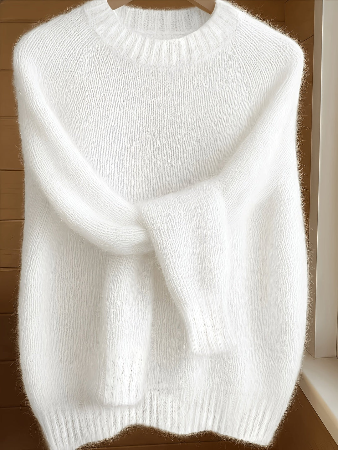 Biały damski sweter z dzianiny wiszący na wieszaku