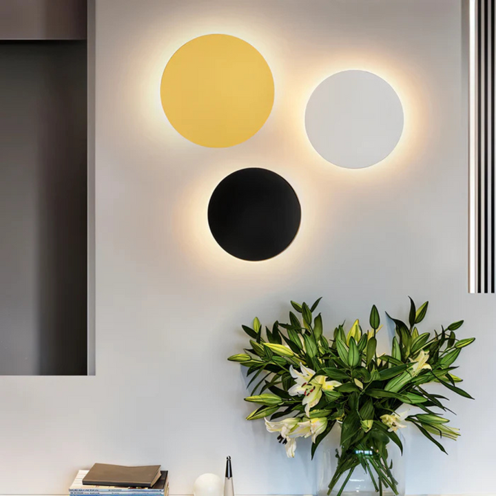 Trzy minimalistyczne lampy ścienne LED w kolorach złotym, czarnym i białym zamontowane na szarej ścianie w eleganckim salonie