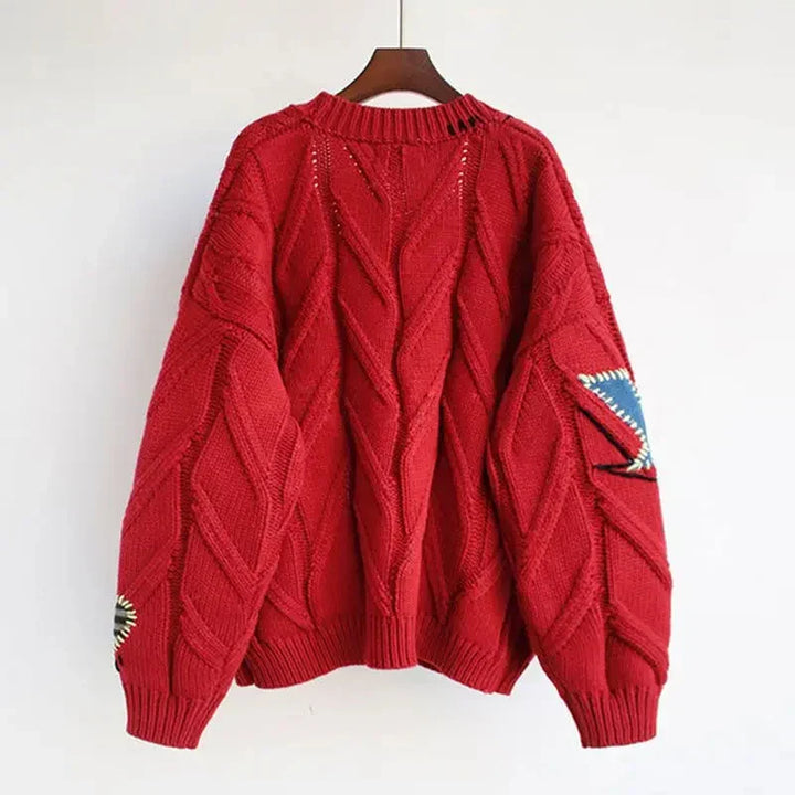 Czerwony damski sweter z haftem patchwork prezentowany na wieszaku
