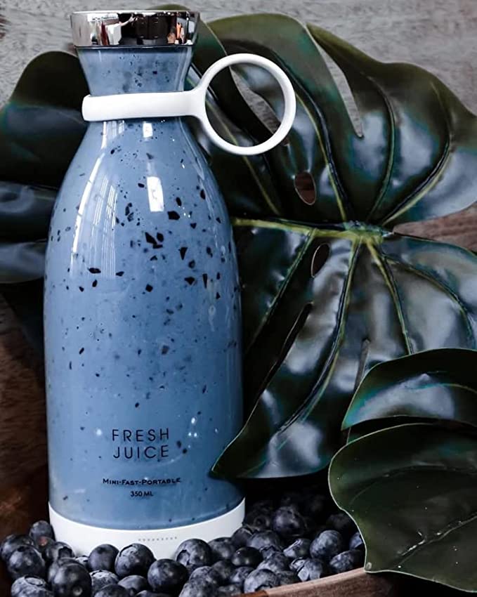 Niebieski bezprzewodowy mini blender na tle zielonych liści