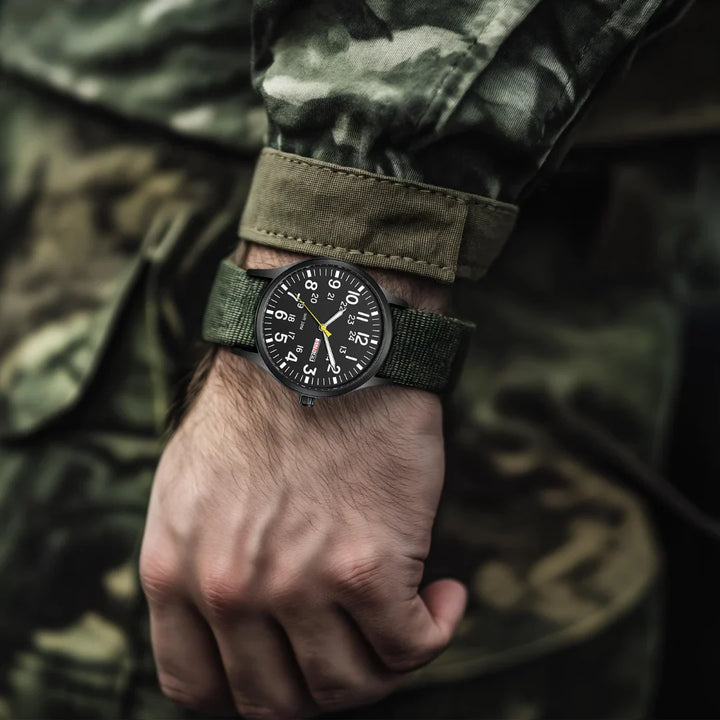 Mężczyzna noszący zielono-czarny zegarek militarny w terenie