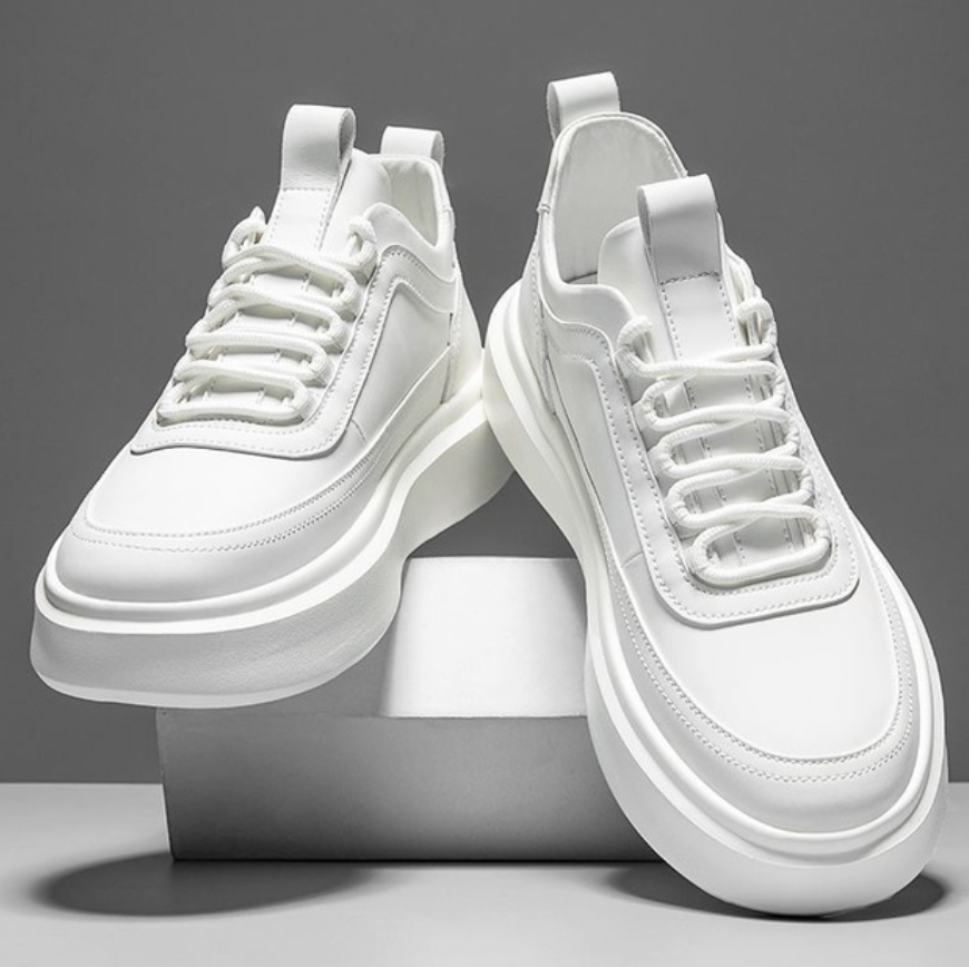 Para białych męskich sneakersów z platformą stojących na białym podwyższeniu
