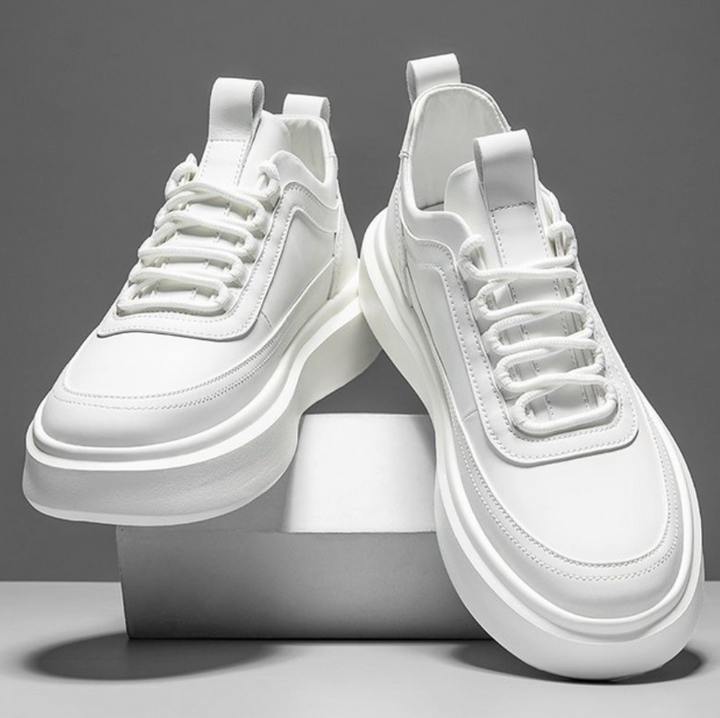 Para białych męskich sneakersów z platformą stojących na białym podwyższeniu