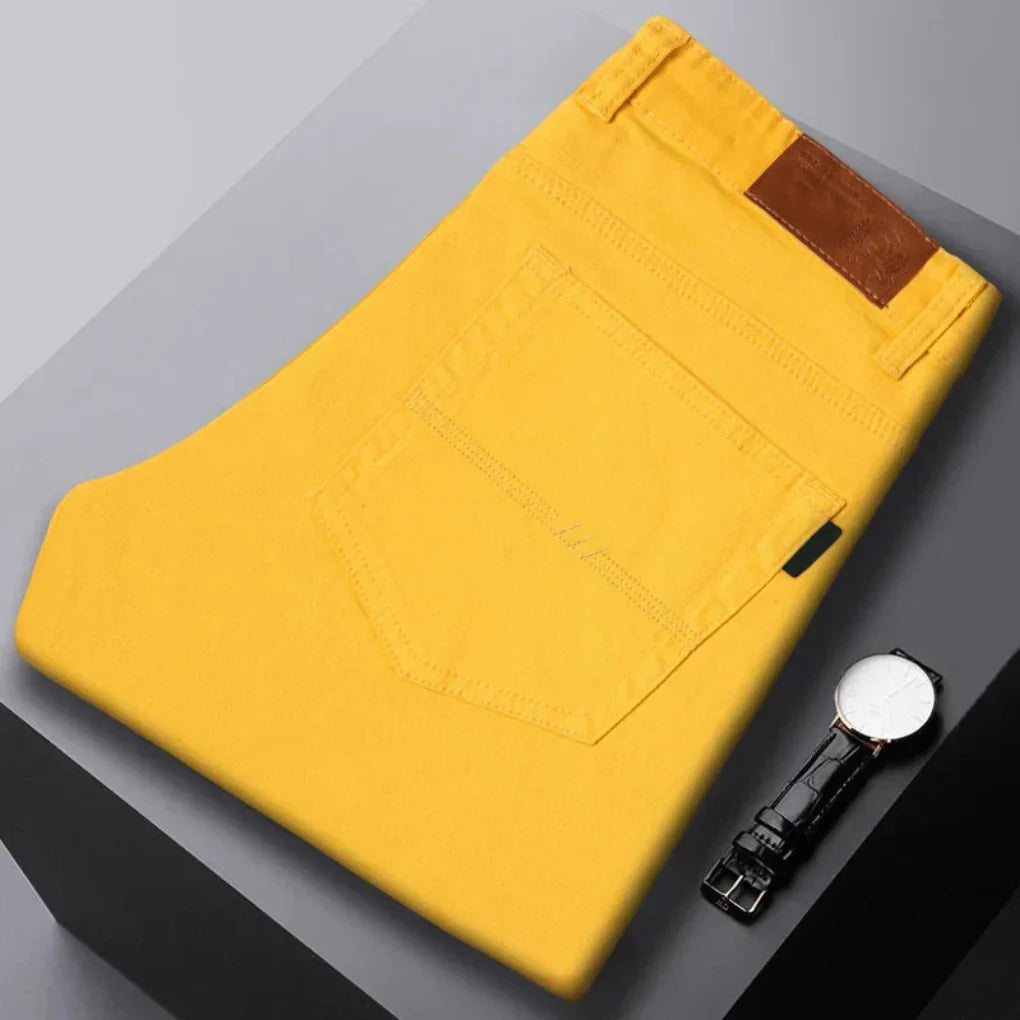 Żółte męskie dżinsy slim fit złożone na stole obok eleganckiego zegarka