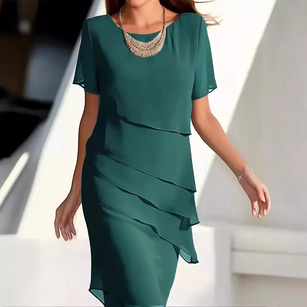 Modelka prezentująca zieloną elegancką sukienkę warstwową z naszyjnikiem