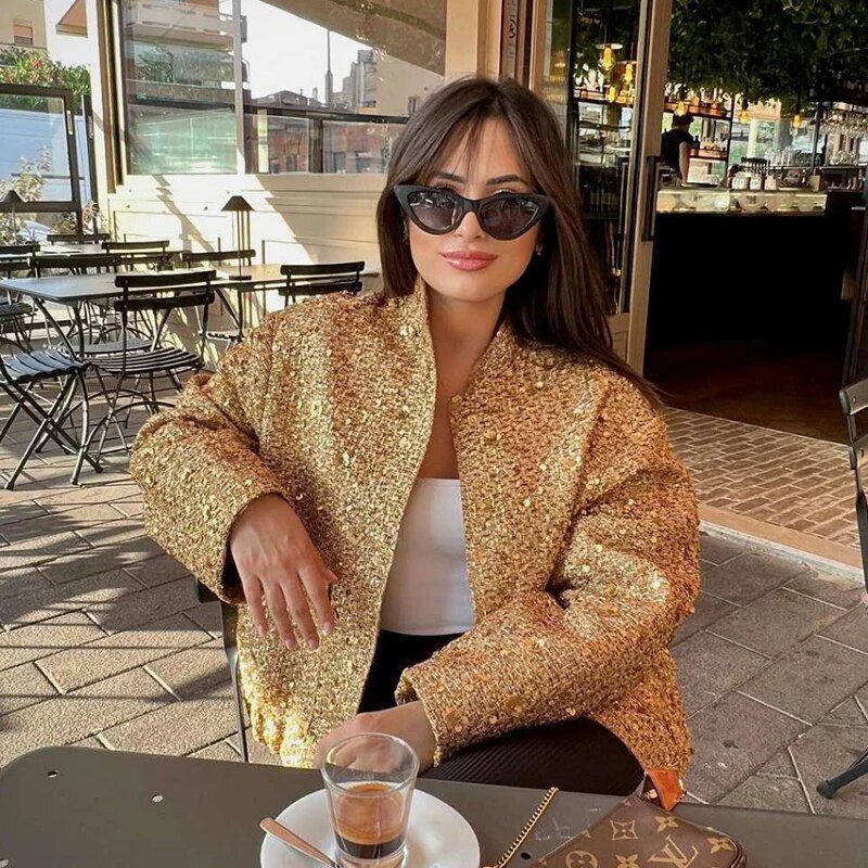 Kobieta w eleganckiej złotej cekinowej kurtce oversize siedząca w kawiarni