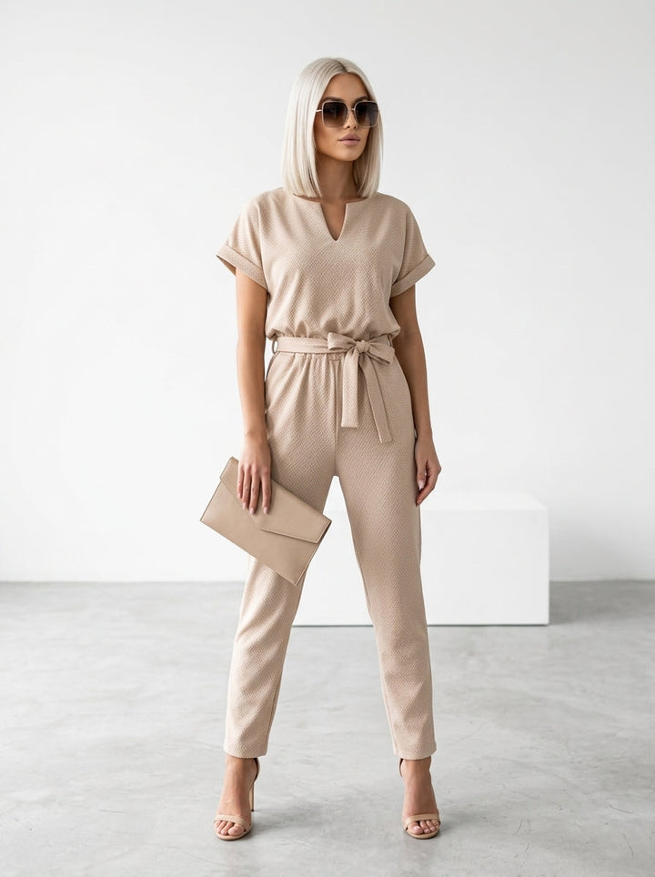Kobieta w beżowo-khaki eleganckim kombinezonie z krótkim rękawem i paskiem