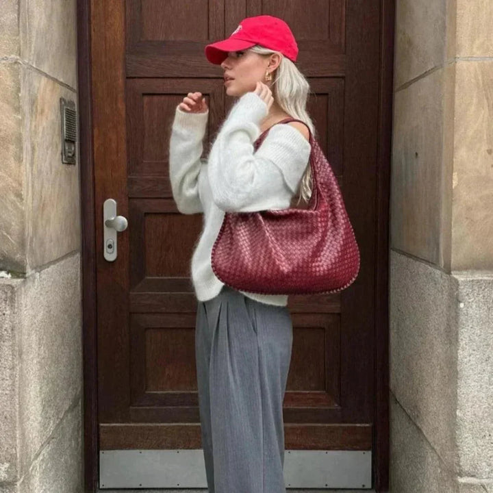 Kobieta prezentująca czerwoną plecioną torebkę Amélie na ramieniu przed drewnianymi drzwiami