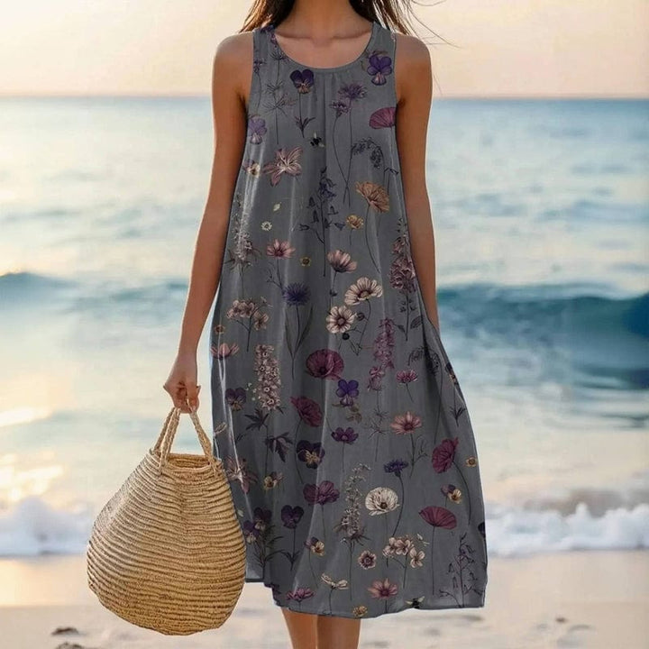 Kobieta w ciemnoszarej sukience plażowej w kwiaty trzymająca torbę na plaży