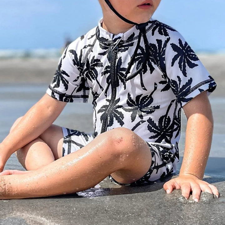 Chłopięcy kostium kąpielowy z palmami i białym czepkiem UV. Idealny na basen i plażę, chroni przed słońcem.