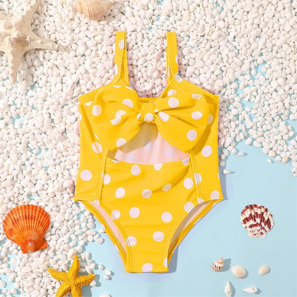 Dziewczęcy strój kąpielowy jednoczęściowy w białe grochy z kokardą. Retro moda dziecięca na plażę i lato.
