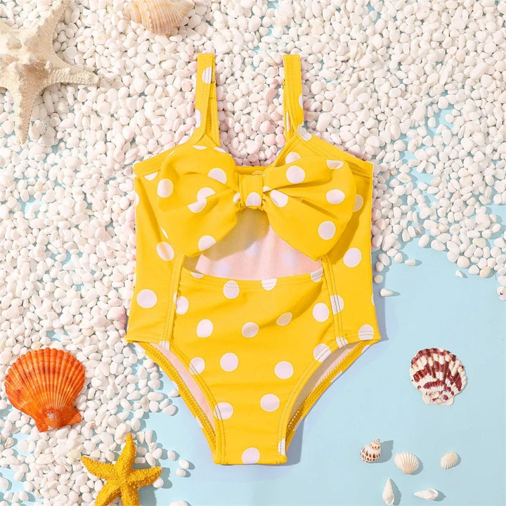 Dziewczęcy strój kąpielowy jednoczęściowy w białe grochy z kokardą. Retro moda dziecięca na plażę i lato.