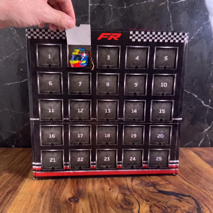 Dłoń otwiera numerowane okienko w czarnym kalendarzu adwentowym Formuła Racing z miniaturką kasku