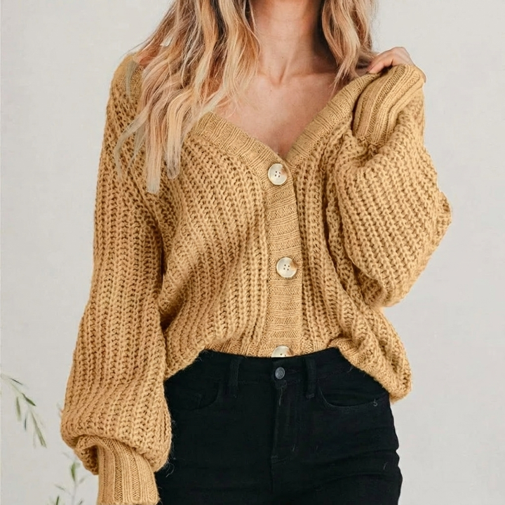 Kobieta ubrana w musztardowo-khaki gruby sweter rozpinany oversize z dekoltem V i guzikami.