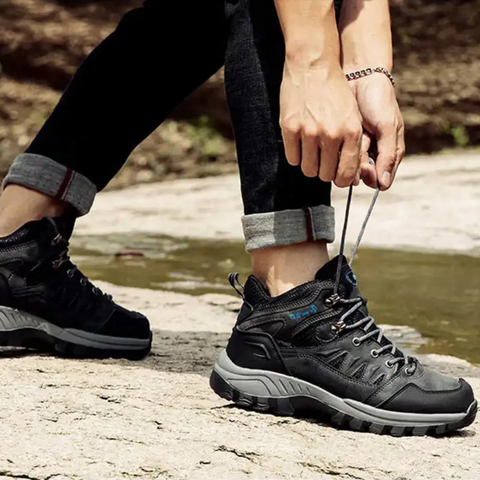 Mężczyzna wiążący czarne wodoodporne buty trekkingowe na tle natury