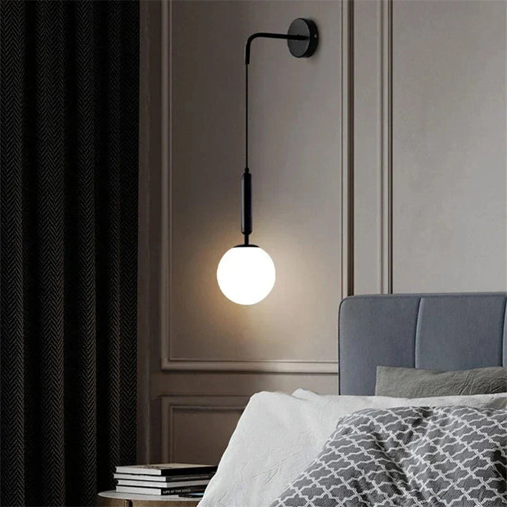 Elegancka lampa ścienna z czarnym ramieniem i szklanym klobusem zamontowana na ścianie