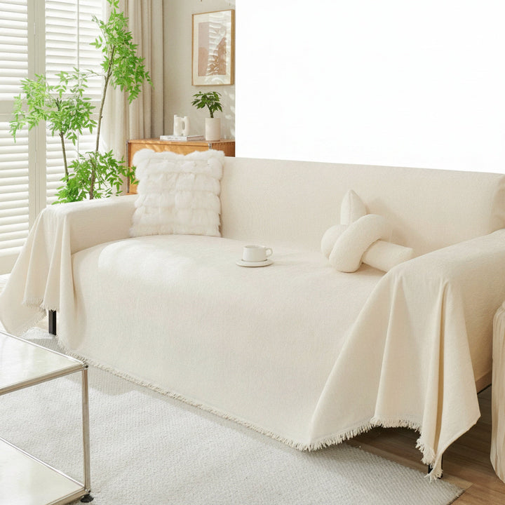 Kremowa narzuta na sofę w stylu boho z frędzlami rozłożona na kanapie w jasnym salonie