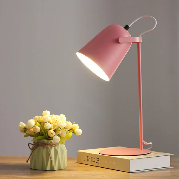 Różowa nordycka lampa stołowa stojąca na biurku obok książki i wazonu z kwiatami