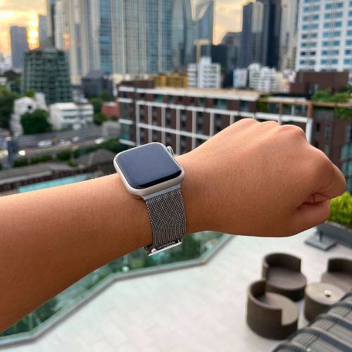 Apple Watch ze srebrną bransoletą Milanese Loop na nadgarstku w miejskiej scenerii
