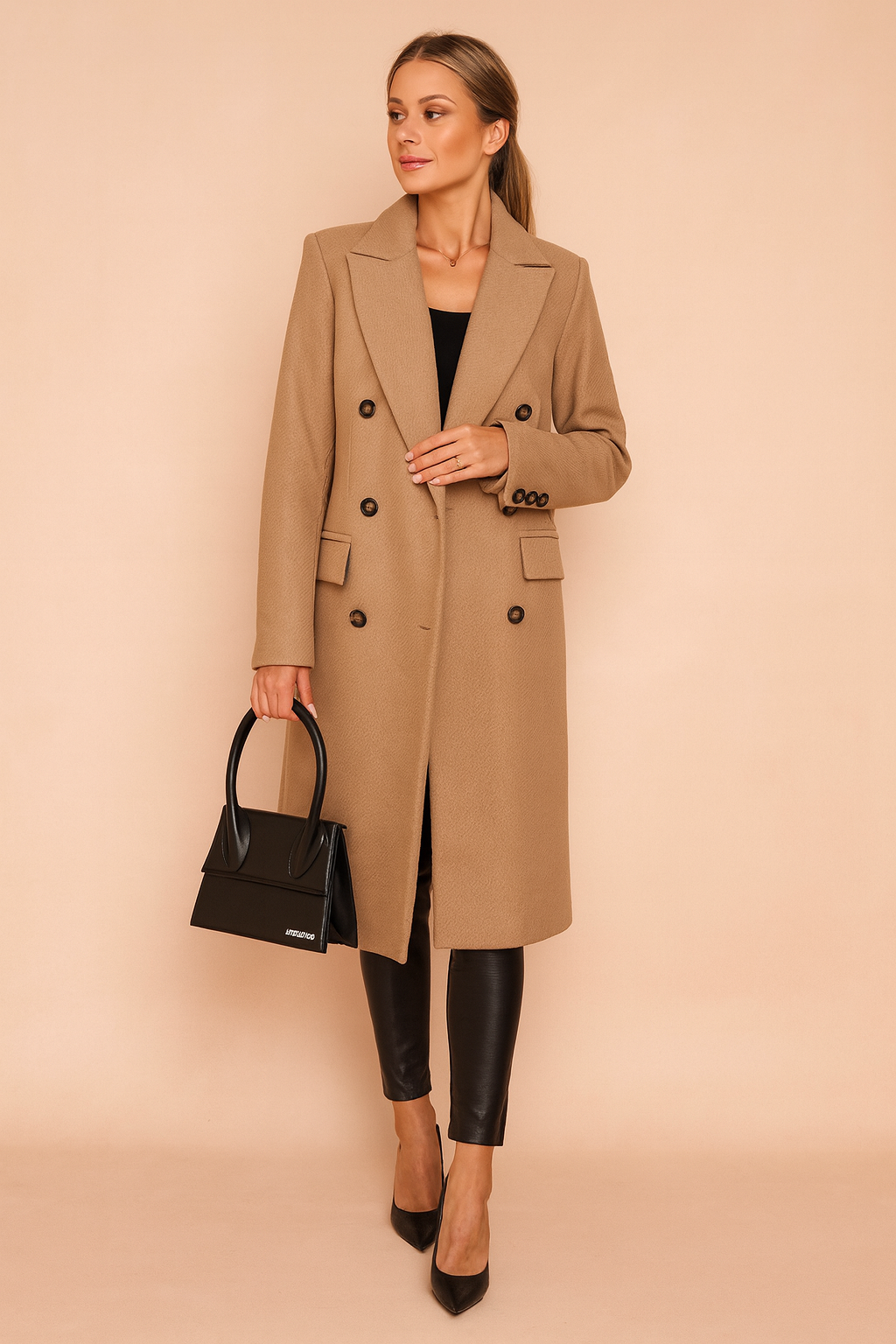 Modelka w eleganckim długim płaszczu zimowym w kolorze khaki, z dwurzędowym zapięciem i czarną torebką w dłoni.