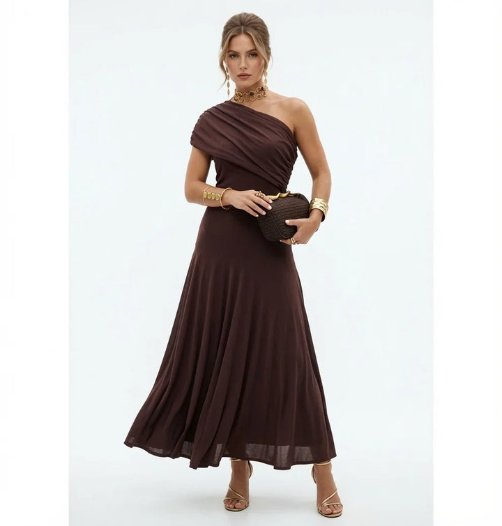 Modelka prezentująca elegancką brązową sukienkę maxi na jedno ramię z torebką