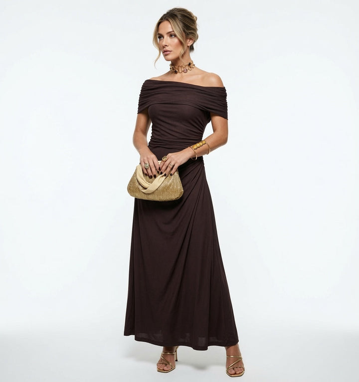 Modelka w brązowej plisowanej sukience maxi trzymająca elegancką torebkę